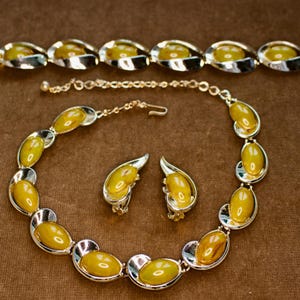 May include: A vintage jewelry set featuring a necklace, bracelet, and earrings. The set includes oval-shaped, yellow-toned stones set in silver-colored metal. The necklace and bracelet have a similar design, while the earrings are clip-on style.
