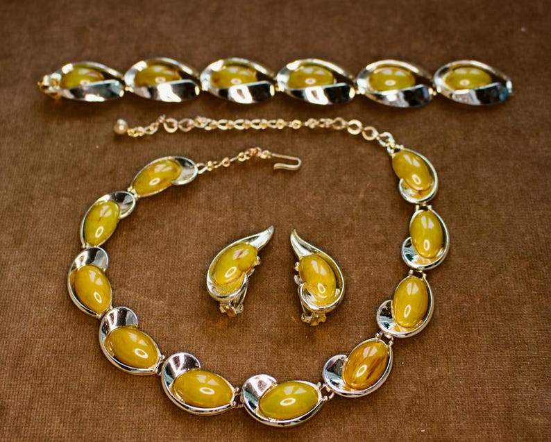 May include: A vintage jewelry set featuring a necklace, bracelet, and earrings. The set includes oval-shaped, yellow-toned stones set in silver-colored metal. The necklace and bracelet have a similar design, while the earrings are clip-on style.
