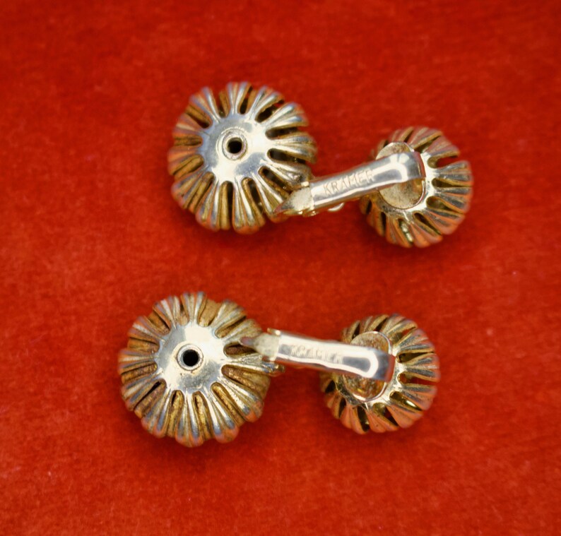Puede incluir: Un par de gemelos vintage con un dise&ntilde;o floral. Los gemelos tienen una base de metal plateado con detalles dorados. El dise&ntilde;o es una serie de p&eacute;talos que irradian desde un punto central. Los gemelos est&aacute;n sobre un fondo rojo.