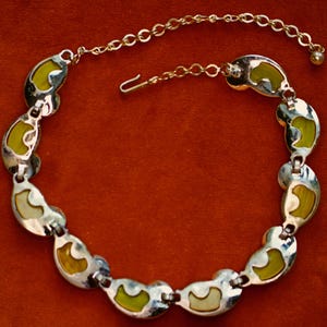 May include: A vintage necklace with a silver-tone metal chain and links. Each link features a kidney-shaped design with a lime green and cream-colored enamel inlay. The necklace has a hook clasp and an extender chain.