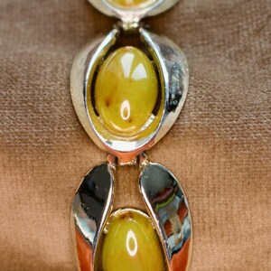 May include: A vintage bracelet featuring three oval, olive-green cabochon stones set in silver-toned metal. The bracelet's design includes a series of stylized, openwork links. The stones have a slight marbling effect, adding depth to the piece.