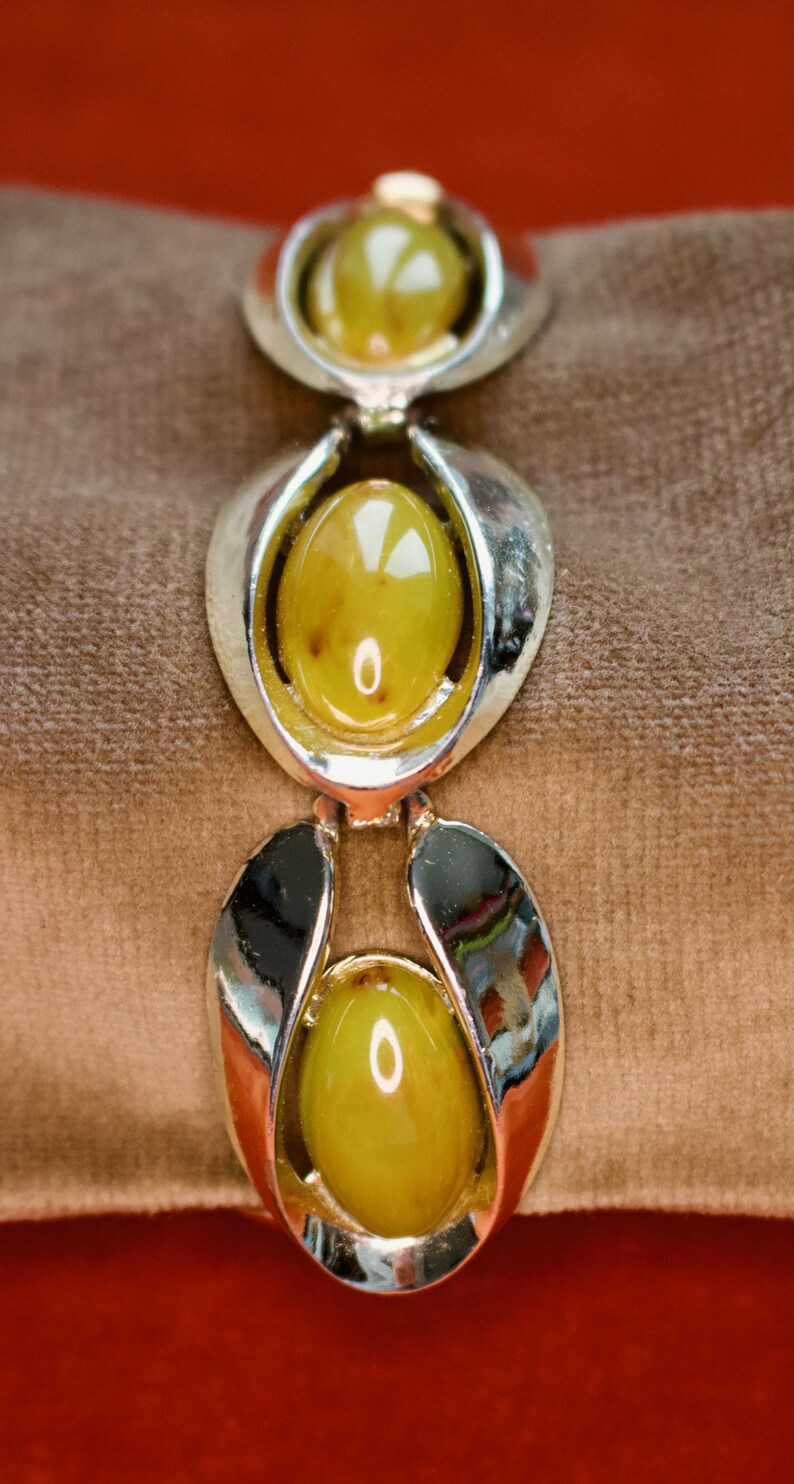May include: A vintage bracelet featuring three oval, olive-green cabochon stones set in silver-toned metal. The bracelet's design includes a series of stylized, openwork links. The stones have a slight marbling effect, adding depth to the piece.