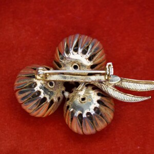 Puede incluir: Broche vintage con tres elementos esf&eacute;ricos plateados y texturizados. El broche tiene un cierre de alfiler y detalles decorativos en forma de hojas. El broche est&aacute; sobre un fondo rojo.