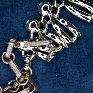 May include: Silver-toned necklace with a decorative floral design. The necklace features a chain and a clasp with the brand name "FISHER" visible. The design includes multiple linked elements.