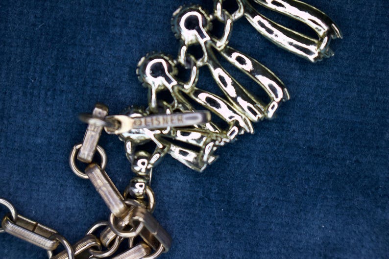 May include: Silver-toned necklace with a decorative floral design. The necklace features a chain and a clasp with the brand name "FISHER" visible. The design includes multiple linked elements.