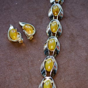 May include: A vintage jewelry set featuring a bracelet and matching earrings. The set has oval, amber-colored stones set in silver-toned metal. The earrings are teardrop-shaped, and the bracelet is composed of linked oval elements.
