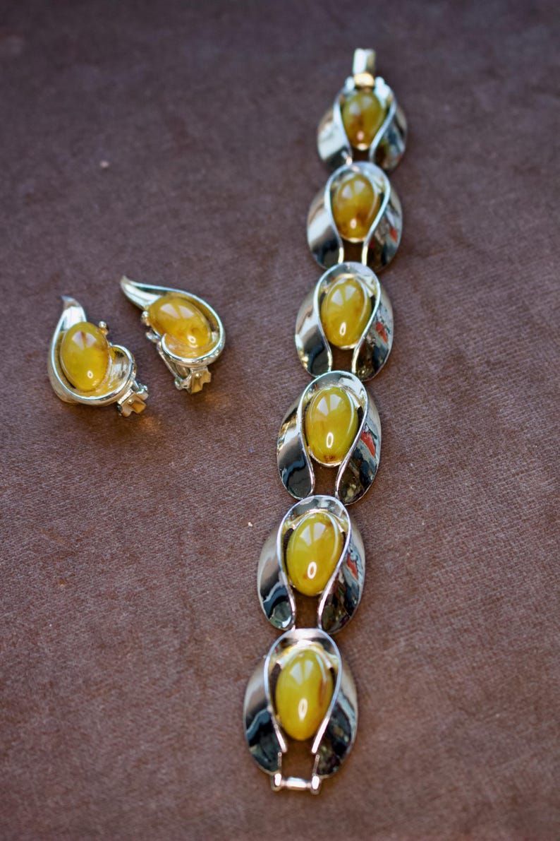 May include: A vintage jewelry set featuring a bracelet and matching earrings. The set has oval, amber-colored stones set in silver-toned metal. The earrings are teardrop-shaped, and the bracelet is composed of linked oval elements.