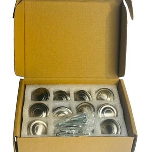 Puede incluir: Un juego de diez pomos redondos para armarios de níquel cepillado, dispuestos en una caja de cartón con inserciones de espuma blanca. Los pomos presentan un diseño circular escalonado. Incluye una bolsa de plástico con tornillos metálicos.