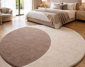 May include: A large circular area rug featuring a two-tone design with a soft, textured pile. One half of the rug is a deep taupe brown, while the other half is a light cream beige, creating a distinct crescent-like color split across the surface.