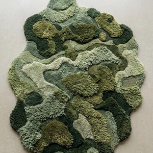 May include: A unique, abstract rug in shades of green, resembling a topographical map or a landscape. The rug features varying textures and pile heights, creating a three-dimensional effect. The design incorporates multiple shades of green, from light to dark.
