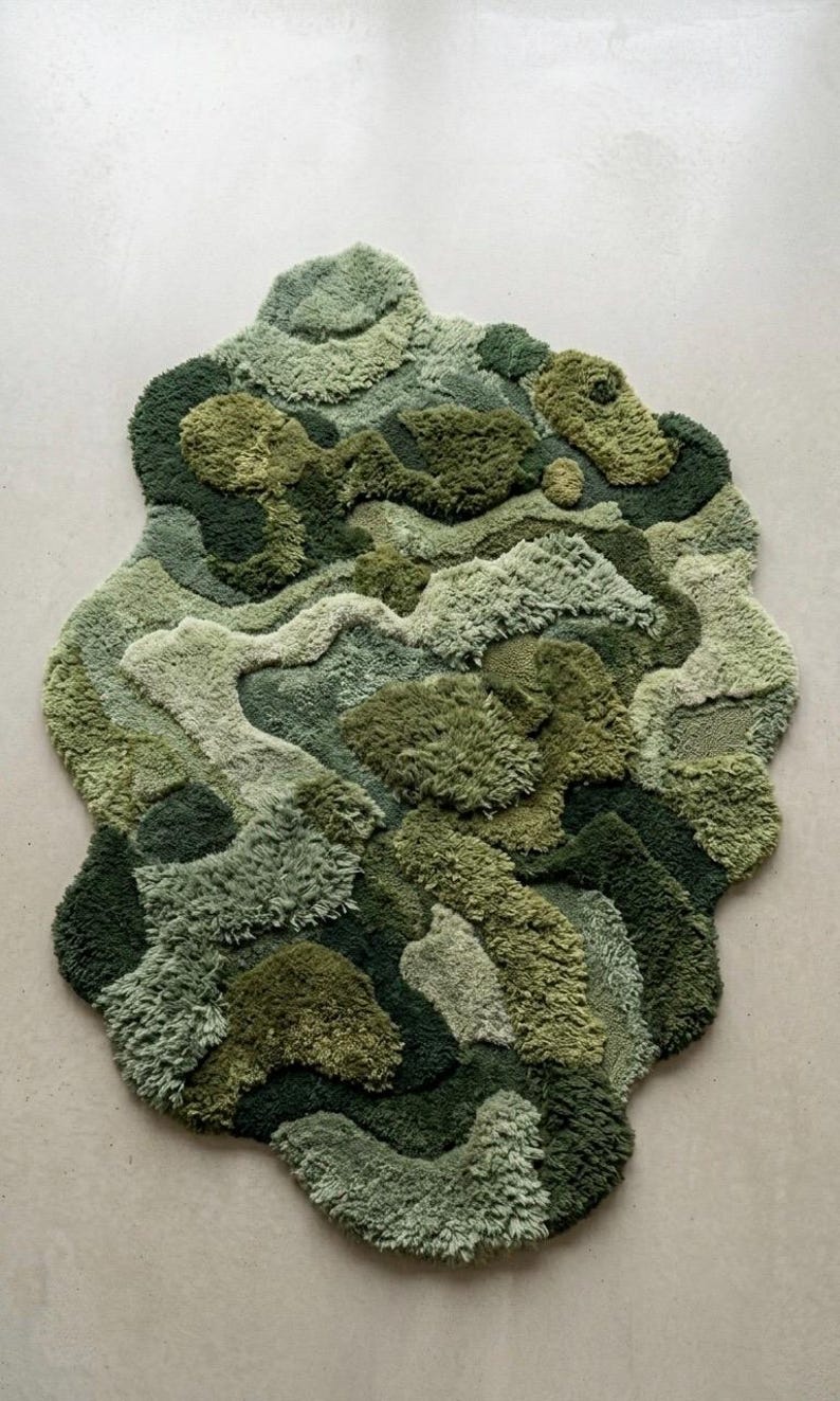 May include: A unique, abstract rug in shades of green, resembling a topographical map or a landscape. The rug features varying textures and pile heights, creating a three-dimensional effect. The design incorporates multiple shades of green, from light to dark.
