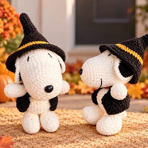 Puede incluir: Dos figuras de perro tejidas a ganchillo en blanco y negro que llevan sombreros puntiagudos negros con bandas amarillas. Cada figura tiene nariz negra, orejas negras y un pequeño chaleco negro. Un sombrero tiene un cascabel dorado.