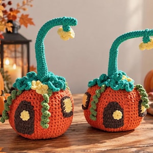 Puede incluir: Dos casas de calabaza tejidas a mano en naranja brillante con puertas marrón oscuro y ventanas amarillas. Cada una tiene un tallo curvo de color verde azulado con una flor amarilla, adornado con volantes y zarcillos verdes.