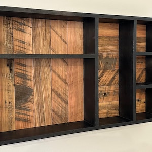 Peut inclure: Étagère murale rectangulaire en bois avec un cadre noir et plusieurs compartiments. L'intérieur présente un motif de grain de bois naturel avec des nuances de marron et d'orange. L'étagère a un aspect rustique et artisanal.