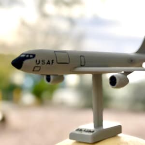 May include: A gray model airplane with the text "USAF" on the side. The model has four engines and is mounted on a stand. The plane's wings are straight, and the tail fin is upright.