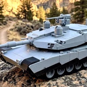 May include: A gray scale model tank featuring a long main gun barrel, a rotating turret with a mounted machine gun, and detailed tracks. The tank has a matte finish with black accents on the lower hull and wheels, showcasing a realistic design.