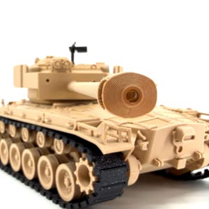 May include: A tan-colored toy tank with black treads and wheels. The tank has a long barrel and a small antenna. The tank is a model of a military vehicle.