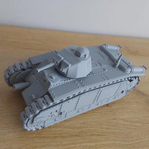 May include: A gray scale model tank featuring a rotating turret with a mounted cannon, a secondary hull-mounted gun, detailed riveted armor plating, and continuous caterpillar tracks on both sides, presented as an unpainted plastic miniature.