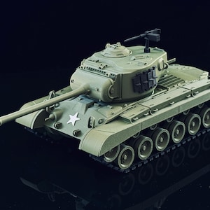 May include: An olive green scale model tank featuring a long main gun barrel, a rotating turret with a mounted black machine gun, and a white star emblem on the front hull. The vehicle is equipped with multiple road wheels and black tracks.