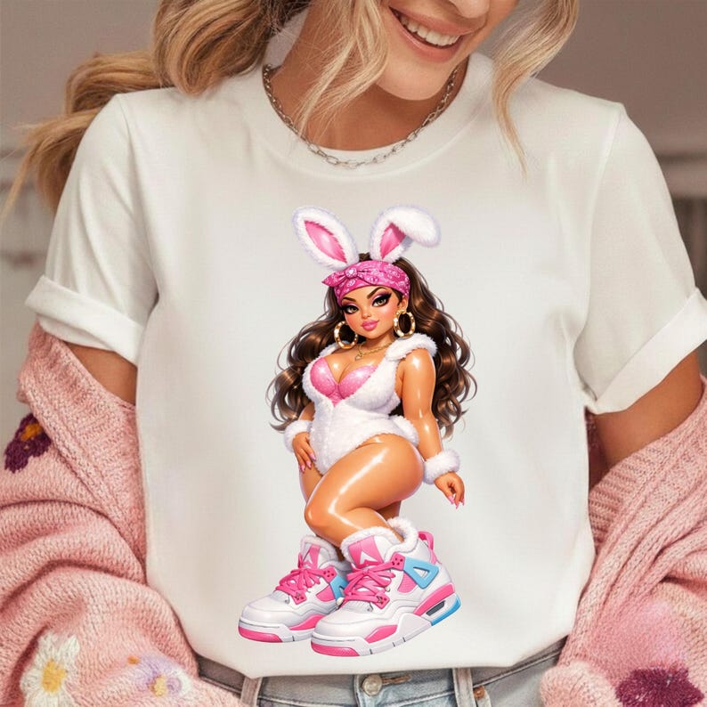 Puede incluir: Una camiseta blanca de manga corta con el gr&aacute;fico de una mu&ntilde;eca de pelo largo casta&ntilde;o, con orejas de conejo blancas, un pa&ntilde;uelo rosa, un body blanco afelpado y zapatillas altas rosas y blancas. La mu&ntilde;eca tiene una piel de aspecto brillante.