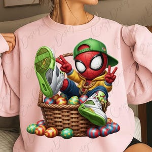 Könnte beinhalten: Rosa Sweatshirt mit einem Cartoon-Spider-Man-Charakter mit grüner Kappe und goldener Kette, der in einem geflochtenen Korb mit bunten Ostereiern sitzt. Die Figur trägt Turnschuhe mit grünen Akzenten. Das Bild hat ein spielerisches und festliches Thema.