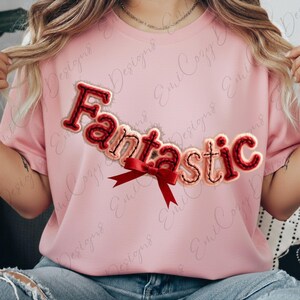 May include: A light pink t-shirt with the word "Fantastic" in a stitched, cursive font. The letters are red and beige with a red bow. The shirt is a casual, everyday wear item.