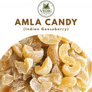 Könnte beinhalten: Ein Haufen durchscheinender, goldgelber Amla-Bonbonstücke, auch bekannt als Indische Stachelbeere, mit einer Zuckerbeschichtung. Über den Bonbons steht der Text VEDIC WILD HERBS, AMLA CANDY und (Indian Gooseberry) mit einem runden Logo.