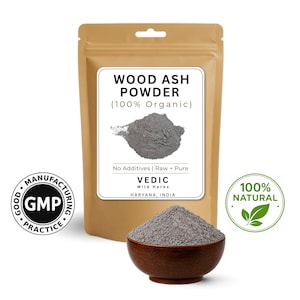Könnte beinhalten: Ein beigefarbener Beutel mit einem weißen Etikett mit der Aufschrift "WOOD ASH POWDER (100% Organic)" und einer grauen Pulverillustration. Eine kleine Holzschale enthält graues Pulver. Das Bild enthält auch ein "100% NATURAL"-Siegel und ein "GMP"-Siegel.