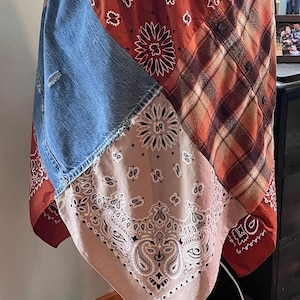 Op de afbeelding: Een patchwork rok met een elastische tailleband, gemaakt van diverse stoffen panelen waaronder blauwe denim met een versleten detail, oranje en bruin geruite flanel, en roestkleurige en beige bandana's met traditionele paisley patronen.