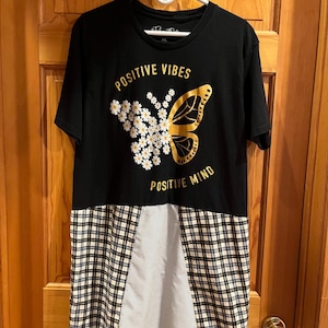 May include: Black t-shirt with a gold butterfly design and the words "POSITIVE VIBES" and "POSITIVE MIND". The bottom half of the shirt is a patchwork of white polka dots and plaid fabric.