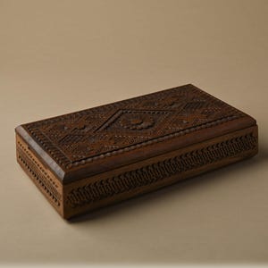 May include: A rectangular dark brown wooden box featuring intricate hand-carved geometric patterns and a central floral motif on the lid. The sides of the box are decorated with a repeating notched border design, showcasing detailed craftsmanship.
