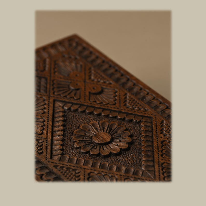 Puede incluir: Una caja de madera de color marr&oacute;n oscuro con intrincados detalles tallados a mano. La superficie muestra un patr&oacute;n geom&eacute;trico repetitivo de diamantes y cuadrados, con un motivo floral central tallado en la madera, con un acabado texturizado en relieve.