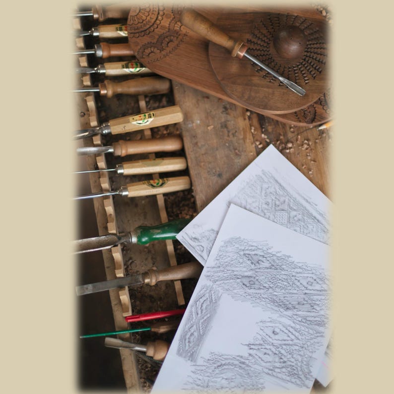 May include: A collection of wood carving tools with wooden handles arranged in a rack, including gouges and chisels. A circular wooden piece with intricate carved patterns and a metal tool rest on top, alongside white papers featuring pencil sketches.