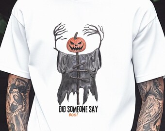 May include: A white short-sleeved t-shirt featuring a graphic of a pumpkin-headed scarecrow with long, spindly arms and a tattered dark cloak. Below the illustration, the text reads DID SOMEONE SAY BOO! in black and orange lettering.