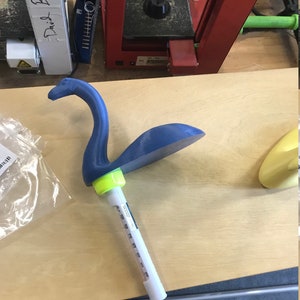 K&ouml;nnte beinhalten: Eine blaue, 3D-gedruckte Nessie-Monsterfigur mit einem gr&uuml;nen Sockel, der an einem wei&szlig;en Thermometer befestigt ist.