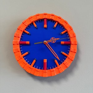 Puede incluir: Una esfera de reloj azul con números y manecillas naranjas. El reloj está rodeado por un marco naranja grueso.