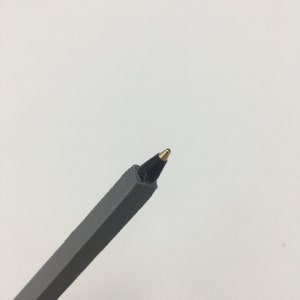 K&ouml;nnte beinhalten: Ein grauer Stift mit einer schwarzen Tintenpatrone und einer goldenen Spitze.