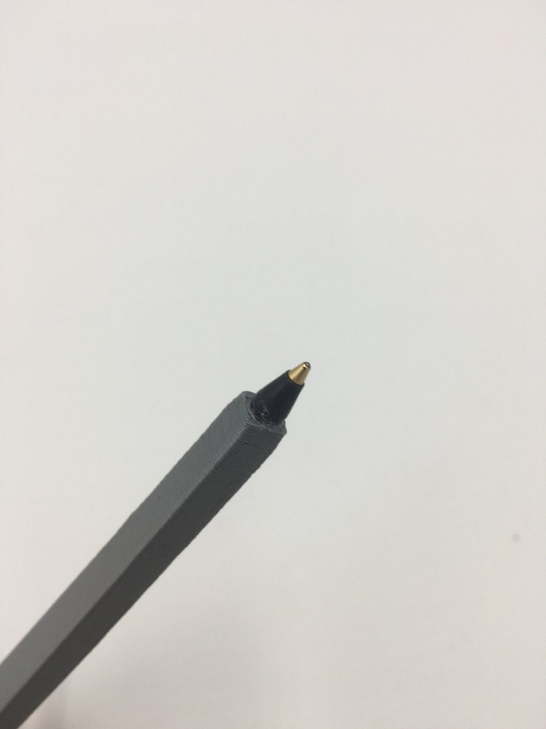 K&ouml;nnte beinhalten: Ein grauer Stift mit einer schwarzen Tintenpatrone und einer goldenen Spitze.