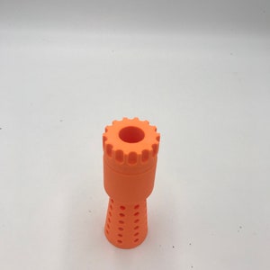 以下が含まれることがあります： オレンジ色のプラスチック製の3Dプリントノズル。歯車のようなトップと、穴の開いた円錐形のボトムがあります。