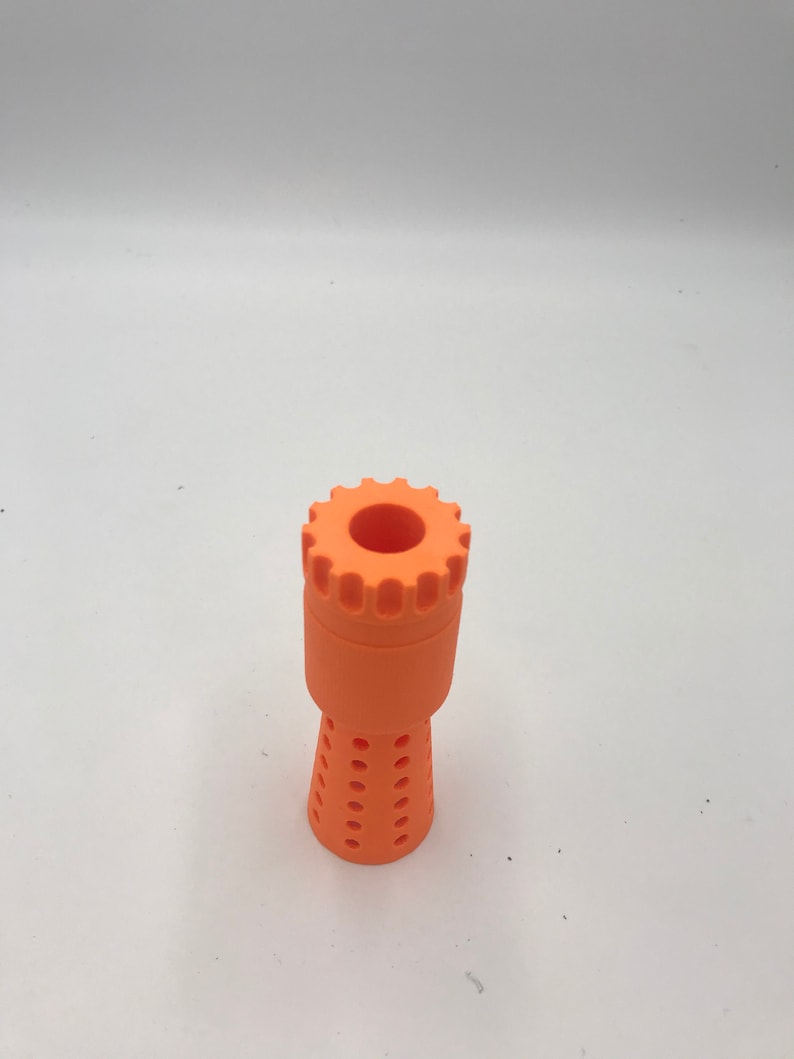 以下が含まれることがあります： オレンジ色のプラスチック製の3Dプリントノズル。歯車のようなトップと、穴の開いた円錐形のボトムがあります。