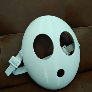 May include: White plastic mask with two large eye holes and a smaller mouth hole. The mask has a white elastic strap.