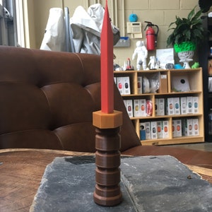 May include: A red and brown plastic knife with a textured handle. The knife is sitting on a wooden table.