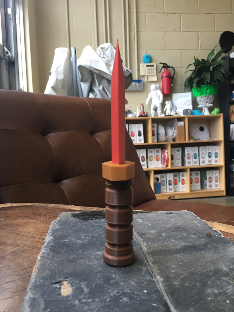 May include: A red and brown plastic knife with a textured handle. The knife is sitting on a wooden table.