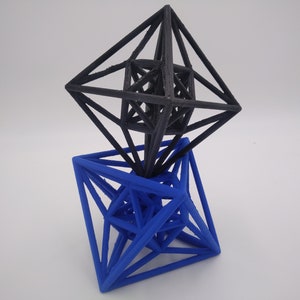 May include: A black geometric shape sits on top of a blue geometric shape. Both shapes are made of wire and appear to be 3D printed.