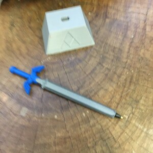 May include: A blue plastic sword with a silver blade and a white plastic stand with a triangular design.