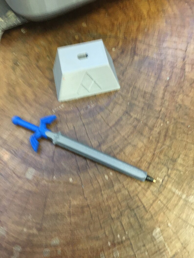 May include: A blue plastic sword with a silver blade and a white plastic stand with a triangular design.