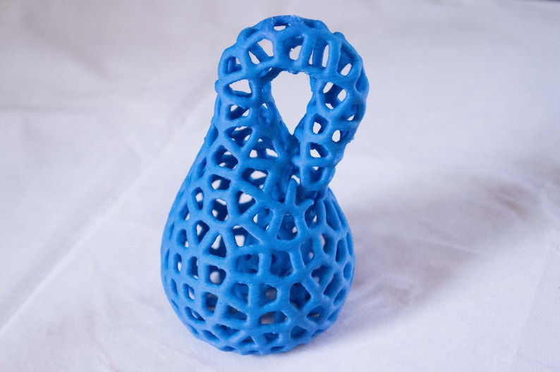 May include: A blue 3D printed vase with a lattice design. The vase has a unique shape with a loop at the top.
