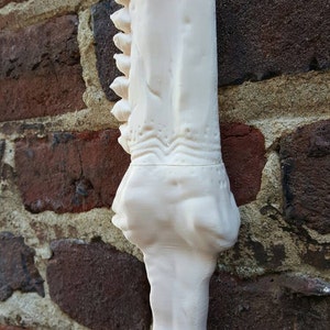 May include: A white 3D printed model of a dinosaur jawbone. The jawbone is detailed with teeth and bone texture.