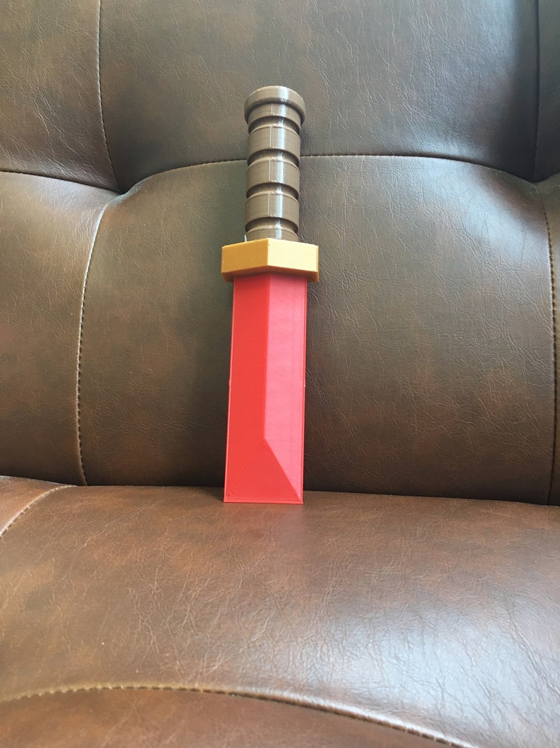 May include: A red plastic toy sword with a brown plastic handle. The sword has a gold-colored hilt.