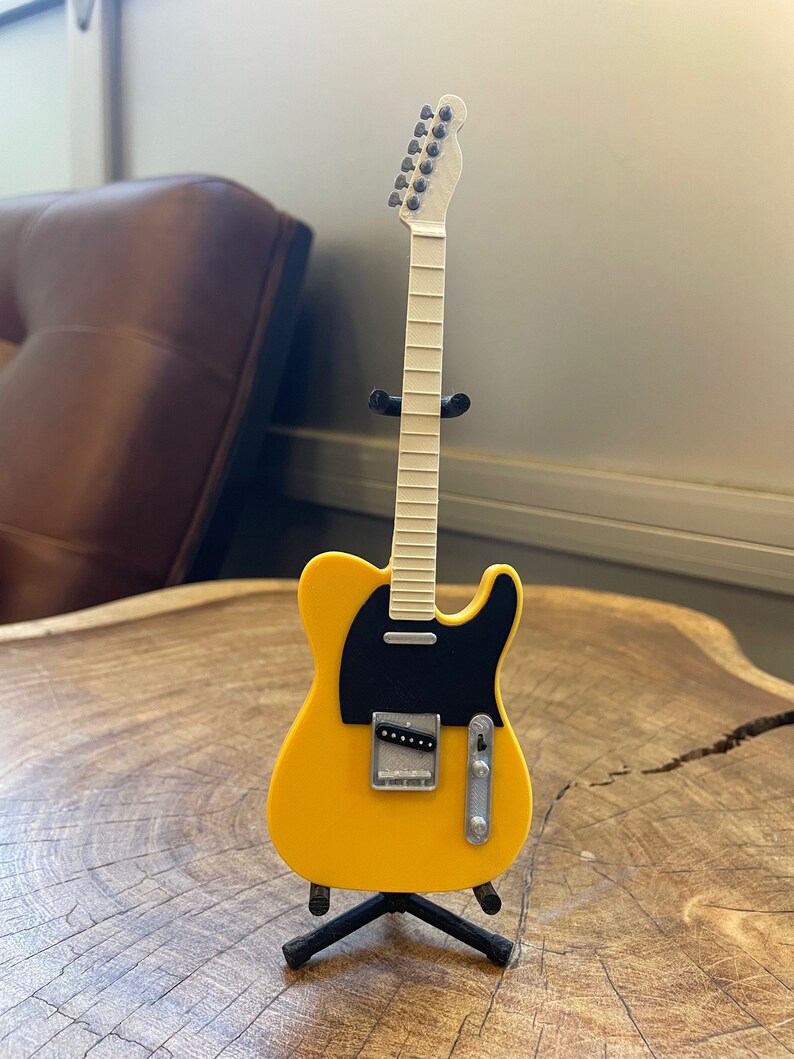 May include: A yellow electric guitar with a black pickguard and a white neck. The guitar is on a black stand.
